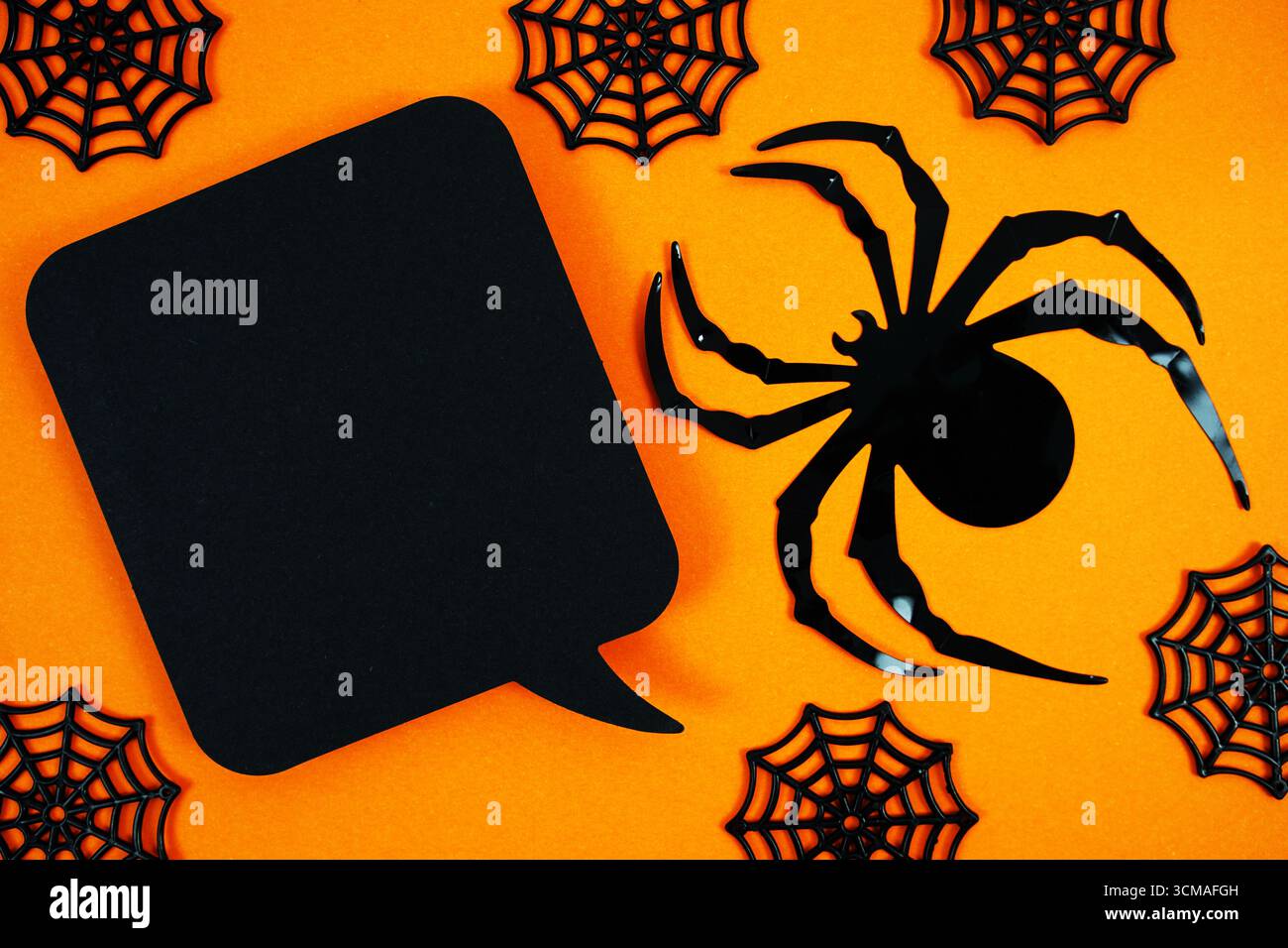 Gruselige orangefarbene Kulisse mit schwarzen Spinnennetzen, einer großen Spinne und einer leeren Sprechblase für Halloween-Nachrichten, Partyeinladungen oder thematische Werbeaktionen. Stockfoto
