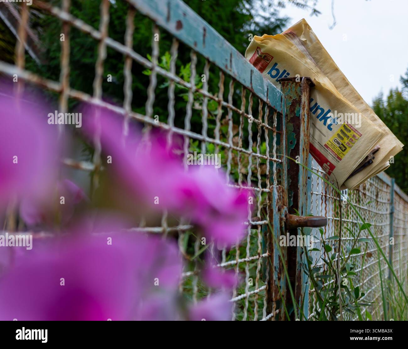 Alte Zeitung steckt im Rusty Fence des verlassenen Eigentums als Symbol des Niedergangs der Printmedien fest Stockfoto