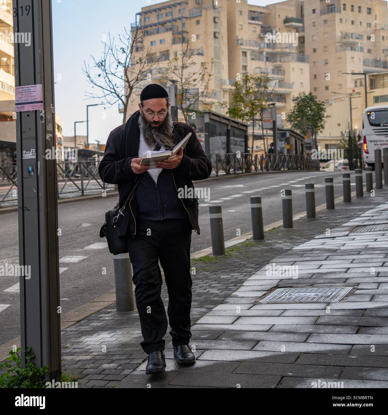 Jerusalem, Israel - 20. Januar 2025: Ein orthodoxer jüdischer Mann liest religiöse Literatur, während er auf einer Jerusalem-Straße spaziert. Stockfoto