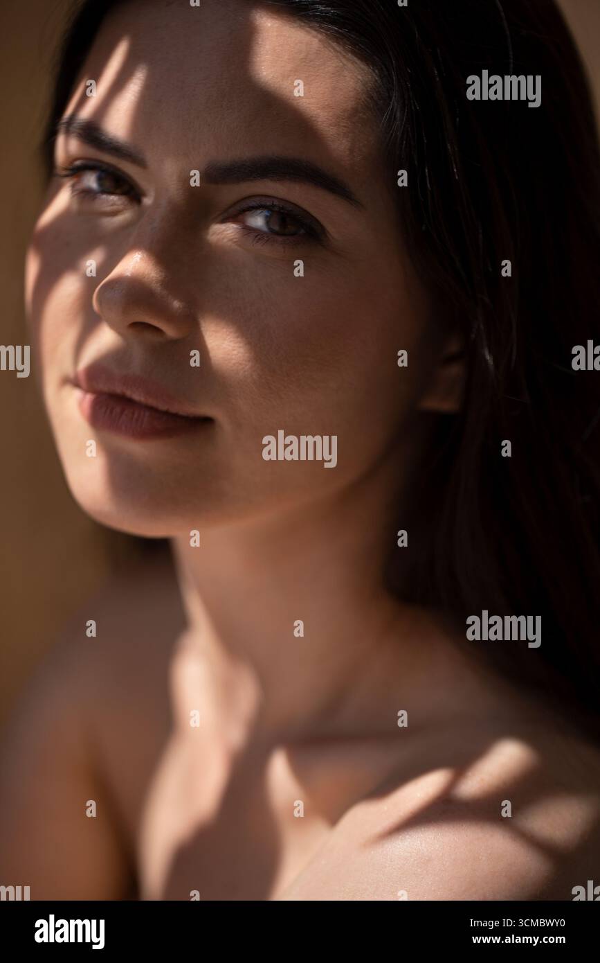 Junge Frau mit langen dunklen Haaren, gefangen in weichem natürlichem Licht, erzeugt sanfte Schatten auf ihrem Gesicht, reflektiert Ruhe und Schönheit in einer friedlichen Umgebung Stockfoto
