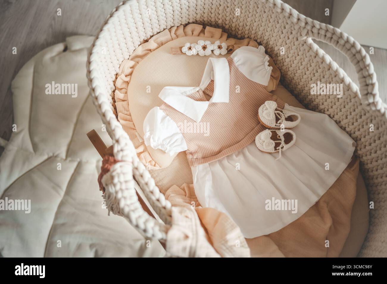 Babykleidung und Accessoires, Kleid und handgefertigte Strickschuhe in der Wiege. Modeartikel für Neugeborene, Draufsicht. Stockfoto