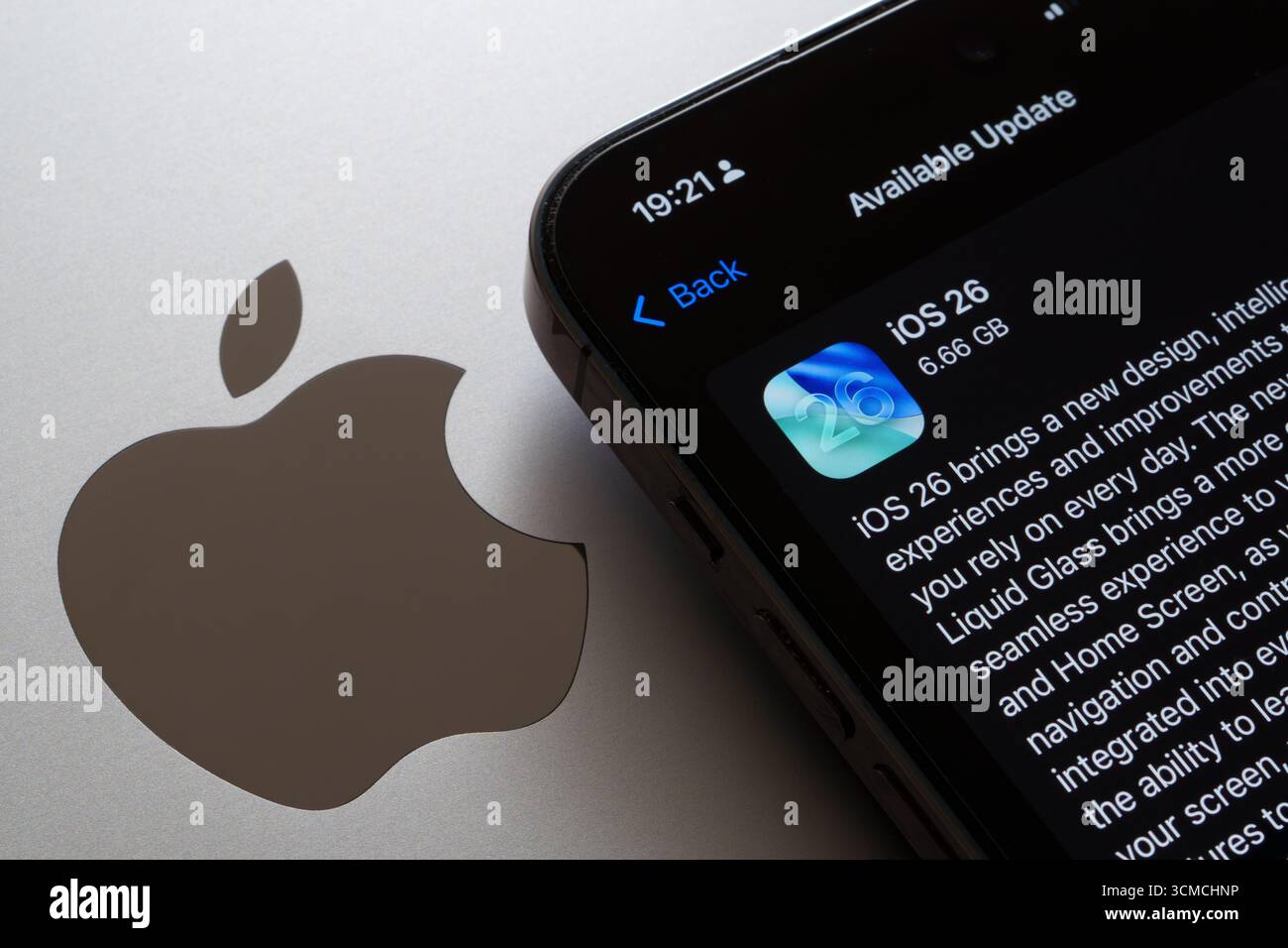 Angewinkeltes iPhone mit Aktualisierung des iOS 26-Modus neben dem großen Apple-Logo auf dem makelgrauen MacBook. Stafford, Vereinigtes Königreich, 15. September 2025 Stockfoto