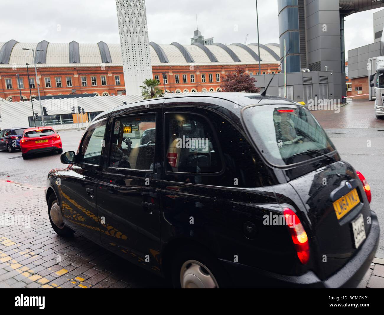 Manchester, Großbritannien - 14. September 2025: Schwarzes Taxi fährt auf einer nassen Stadtstraße in Manchester, Großbritannien Stockfoto