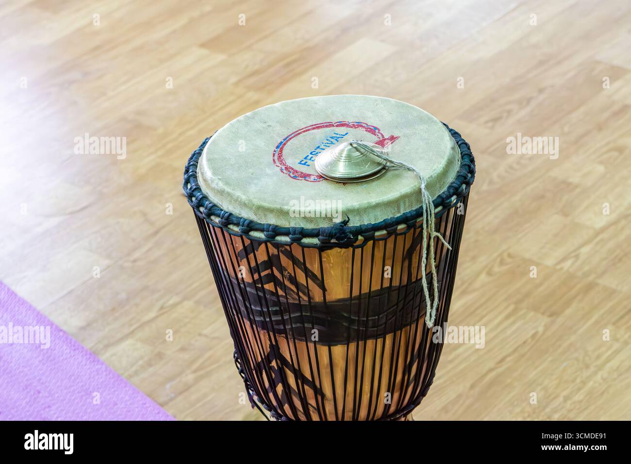 Eine kleine Trommel mit einem Metallstück und schwarzen Seilen um sie herum steht aufrecht auf einem Holzboden. Es wird verwendet, um Rhythmus und Klang während der Gruppensingi hinzuzufügen Stockfoto