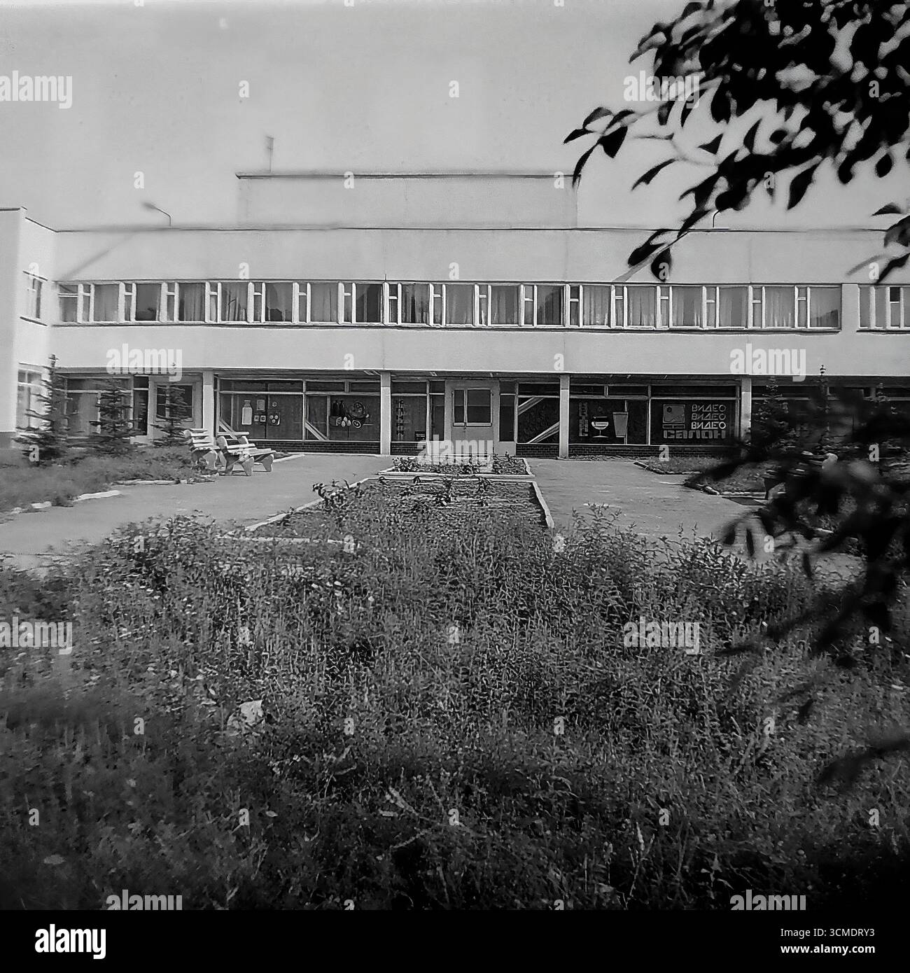 Dieses einzigartige Schwarzweiß-Archivfoto aus dem Jahr 1987 ist eine perfekte Darstellung der Perestroika-Ära in Slowiansk, Ukrainische SSR. Es zeigt das Restaurant „Vesna“ (Frühling) im Wohnviertel Artyom. In den Fenstern sind die Schilder für einen „Videosalon“ zu sehen, eine der ersten Formen privater Genossenschaften in der UdSSR und ein Symbol für die kommende westliche Massenkultur. Diese Szene fängt perfekt den Geist der Zeit ein, in der die sowjetische Infrastruktur neue kommerzielle Unternehmungen beherbergen konnte, was die sozialen und wirtschaftlichen Veränderungen in den letzten Jahren der Sowjetunion signalisierte Stockfoto