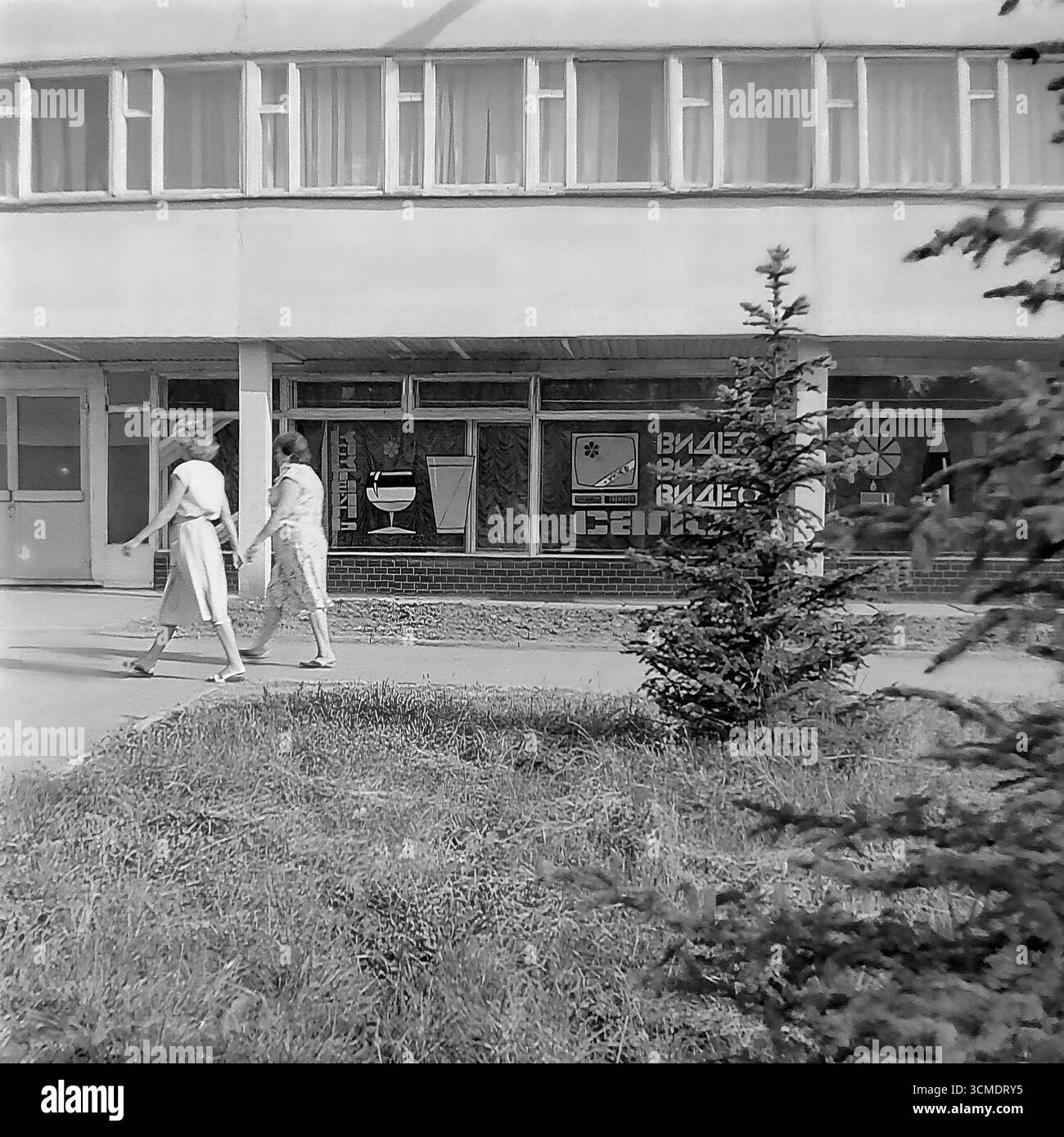 Dieses einzigartige Schwarzweiß-Archivfoto aus dem Jahr 1987 ist eine perfekte Darstellung der Perestroika-Ära in Slowiansk, Ukrainische SSR. Es zeigt das Restaurant „Vesna“ (Frühling) im Wohnviertel Artyom. In den Fenstern sind die Schilder für einen „Videosalon“ zu sehen, eine der ersten Formen privater Genossenschaften in der UdSSR und ein Symbol für die kommende westliche Massenkultur. Diese Szene fängt perfekt den Geist der Zeit ein, in der die sowjetische Infrastruktur neue kommerzielle Unternehmungen beherbergen konnte, was die sozialen und wirtschaftlichen Veränderungen in den letzten Jahren der Sowjetunion signalisierte Stockfoto