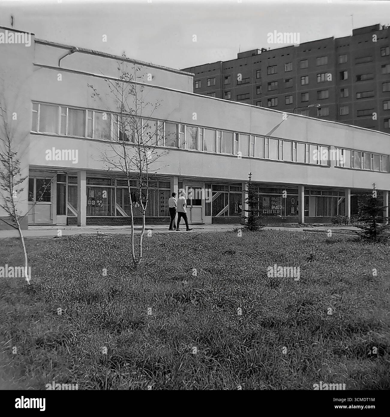 Dieses einzigartige Schwarzweiß-Archivfoto aus dem Jahr 1987 ist eine perfekte Darstellung der Perestroika-Ära in Slowiansk, Ukrainische SSR. Es zeigt das Restaurant „Vesna“ (Frühling) im Wohnviertel Artyom. In den Fenstern sind die Schilder für einen „Videosalon“ zu sehen, eine der ersten Formen privater Genossenschaften in der UdSSR und ein Symbol für die kommende westliche Massenkultur. Diese Szene fängt perfekt den Geist der Zeit ein, in der die sowjetische Infrastruktur neue kommerzielle Unternehmungen beherbergen konnte, was die sozialen und wirtschaftlichen Veränderungen in den letzten Jahren der Sowjetunion signalisierte Stockfoto