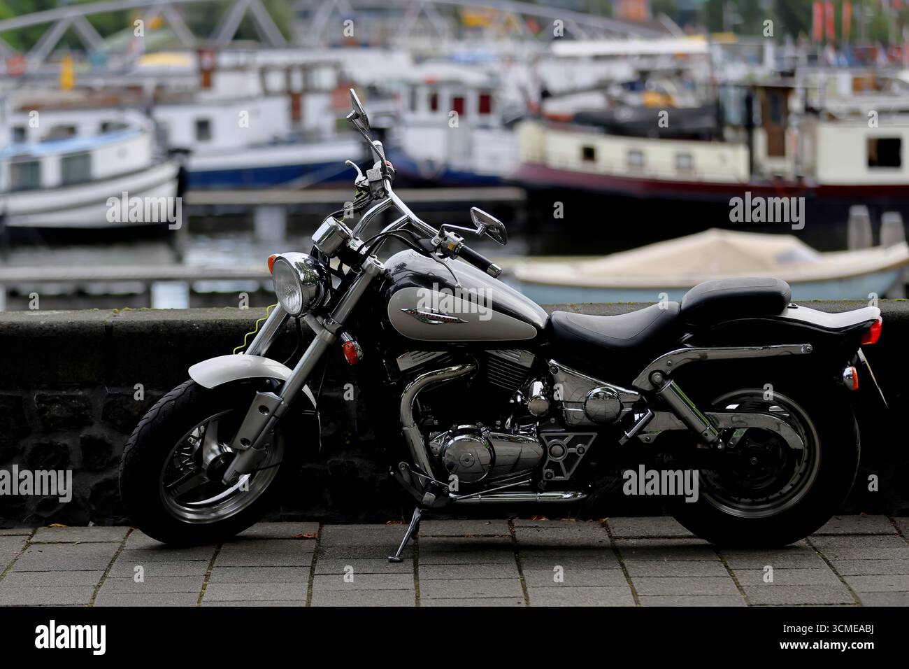 Hyosung Aquila GV650 Cruiser Motorrad auf Pflastersteinen neben verankerten Booten in einem Yachthafen geparkt, Seitenprofil mit Chromdetails und Ständer. Stockfoto