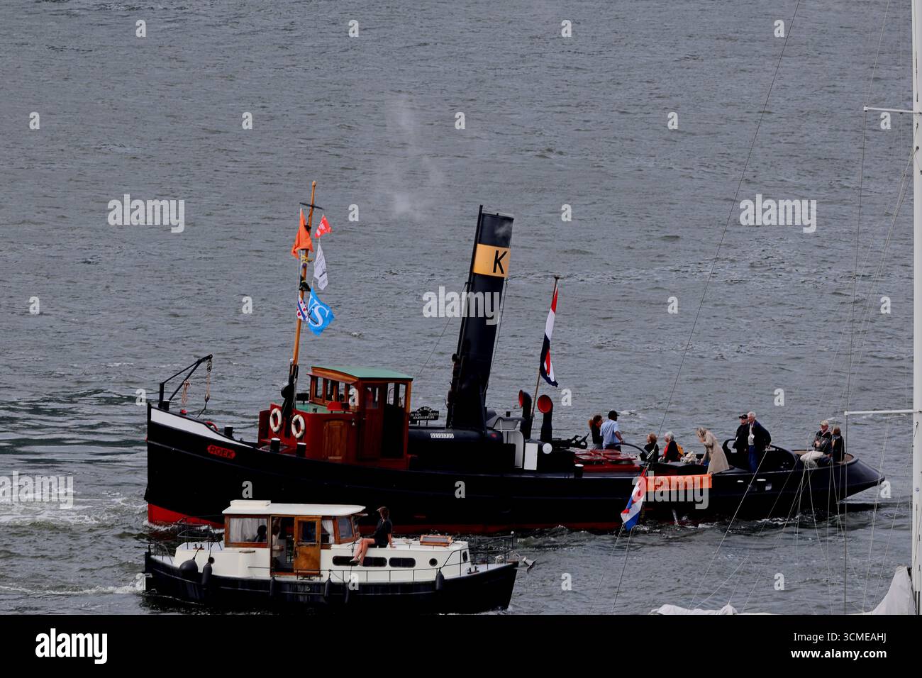 Zwei historische Dampfschlepper fahren zusammen während des Sail 2025 in Amsterdam, Niederlande, mit schwarzen Rümpfen und Schornsteinen, die auf dem städtischen Wasserweg sichtbar sind. Stockfoto Zwei historische Dampfschlepper fahren zusammen während des Sail 2025 in Amsterdam, Niederlande, mit schwarzen Rümpfen und Schornsteinen, die auf dem städtischen Wasserweg sichtbar sind. Stockfoto