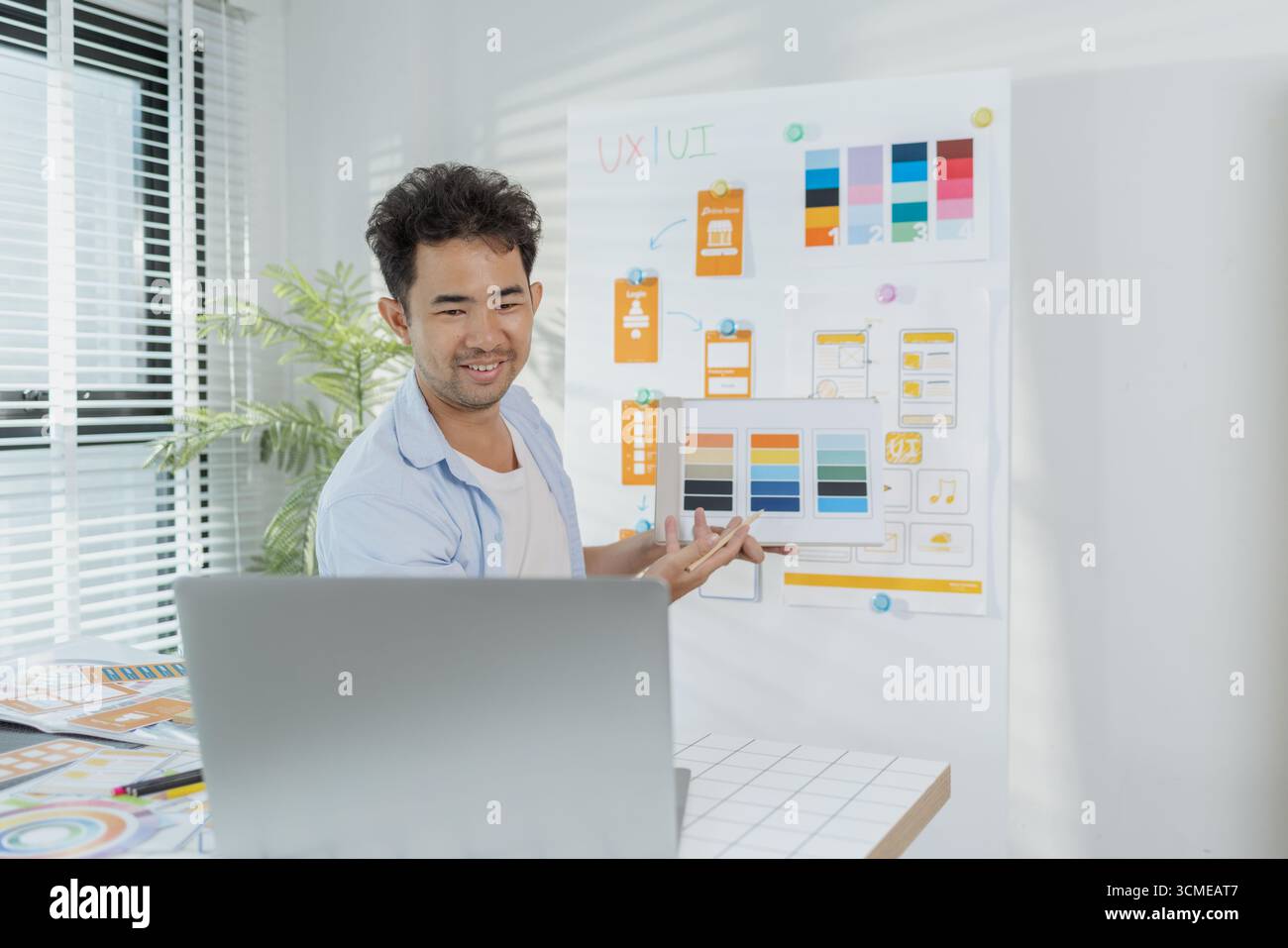 Ein fokussierter Designer arbeitet an UX/UI-Designideen und analysiert Farbpaletten und Schnittstellenstrukturen, die auf einer Platine fixiert sind. Die Szene spiegelt Kreativität wider Stockfoto