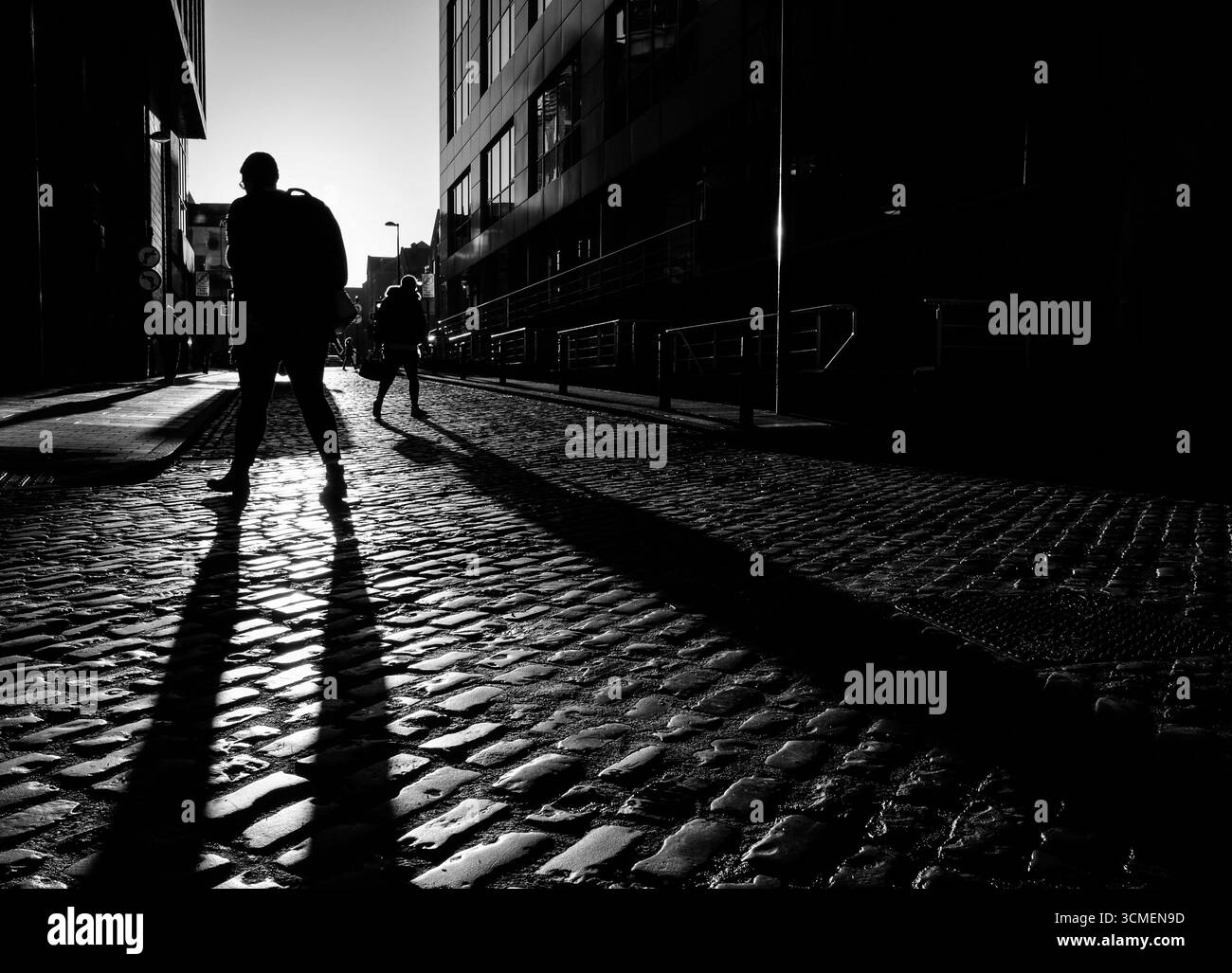 Schwarz-weiße Straßenszene mit Fußgängern und langen Schatten auf Kopfsteinpflaster Stockfoto