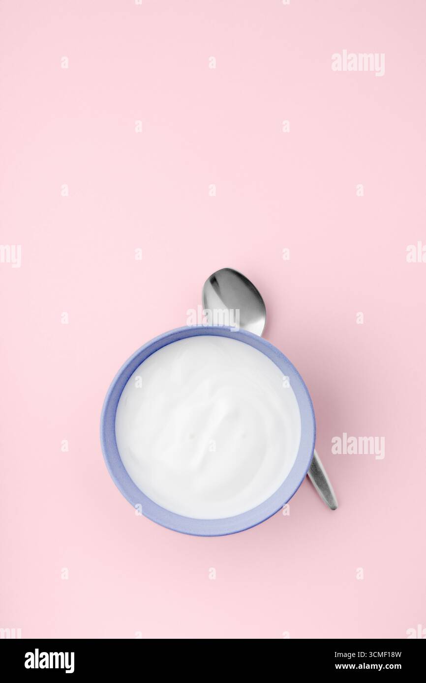 Frischer natürlicher Joghurt in blauer Schüssel auf rosa sauberem Hintergrund Stockfoto
