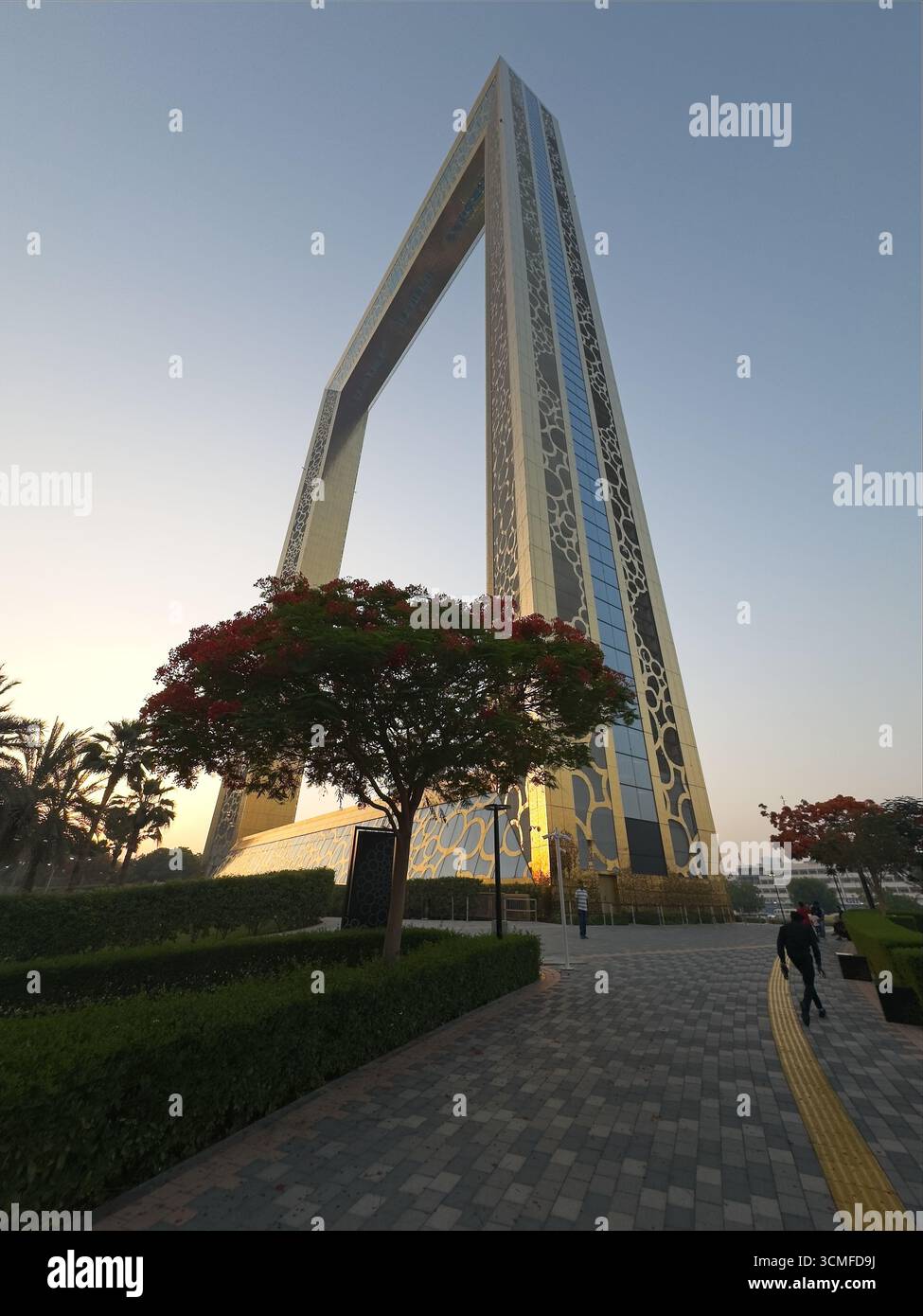Hoch aufragendes, modernes Gebäude mit komplizierten Mustern, umgeben von landschaftlich begrüntem Grün und Wegen. Stockfoto