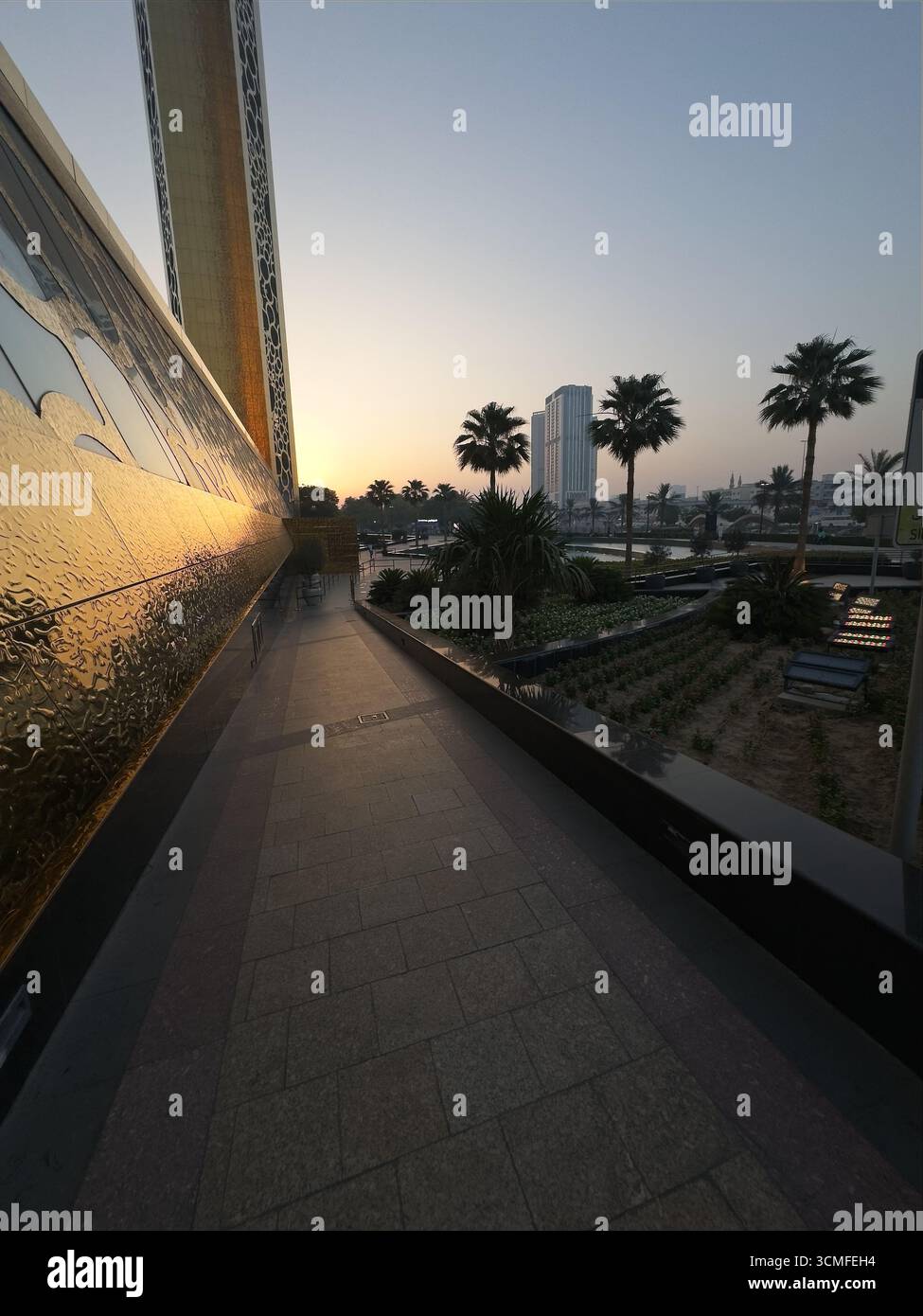 Malerischer Blick auf einen Pfad bei Sonnenuntergang, goldene Reflexe, Palmen und moderne Architektur. Stockfoto