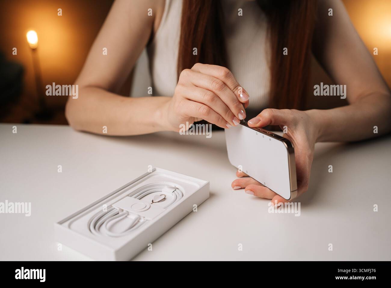 Frau, die einen Metallstift in den sim-Kartensteckplatz des neuen Smartphones einführt und dabei das Auspacken moderner mobiler Geräte präzise und sorgfältig vornimmt. Stockfoto