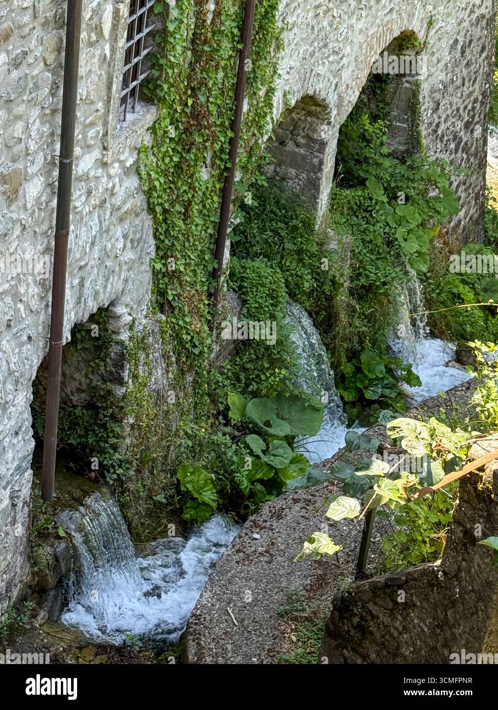 Wasser strömt aus den drei Tunneln einer alten, nicht funktionierenden Wassermühle in den Fiume Rosaro (Fluss Rosaro) in der Provinz Massa-Carrara C a Mo Stockfoto