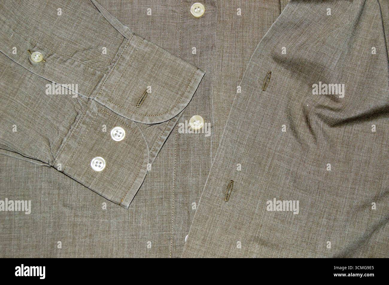 Nahaufnahme eines braungrauen Casual-Herrenhemds, das Ärmelverlauf, weiße Knöpfe, Knopfleisten und eine strukturierte Stofftextur zeigt. Oberansichtshintergrund Stockfoto