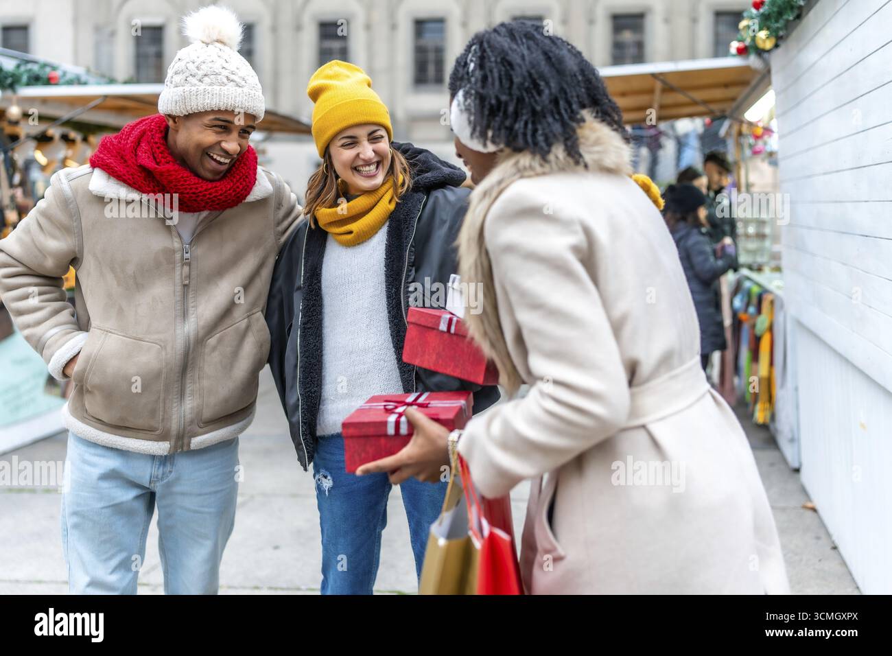 Glückliche Freunde tauschen weihnachtsgeschenke aus, während sie einen Spaziergang durch einen festlichen Wintermarkt genießen Stockfoto