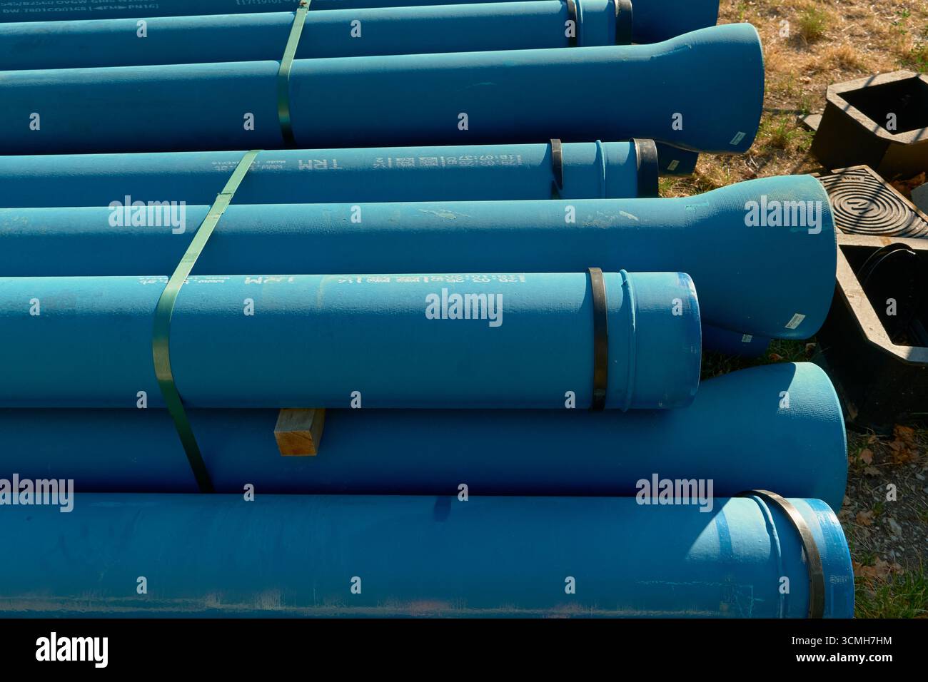 Horizontales Foto von sauber gestapelten blauen Industrierohren und -Röhren unter Sonnenlicht. Helles Ambiente im Freien hebt Texturen, technische Ausstattung und Stockfoto