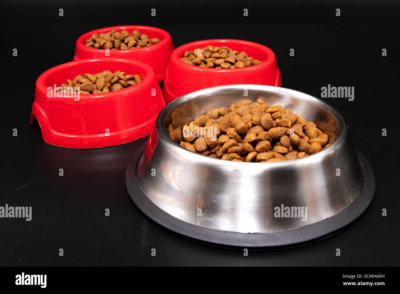 Nahaufnahme von Edelstahl und roten Schalen mit trockenem Tierfutter auf schwarzem Hintergrund. Konzept der Katzen- und Hundefutter, Tierpflege und gesunden Fütterung. Stockfoto