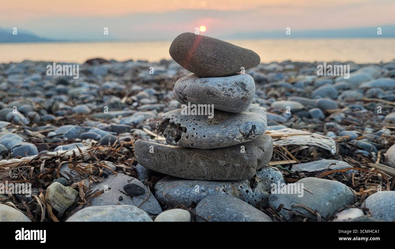 Ein Zen-ähnlicher Stein aus ausgeglichenen Steinen an einem Kiesstrand in Griechenland, der Ruhe und Harmonie bei einem friedlichen Sonnenuntergang symbolisiert Stockfoto