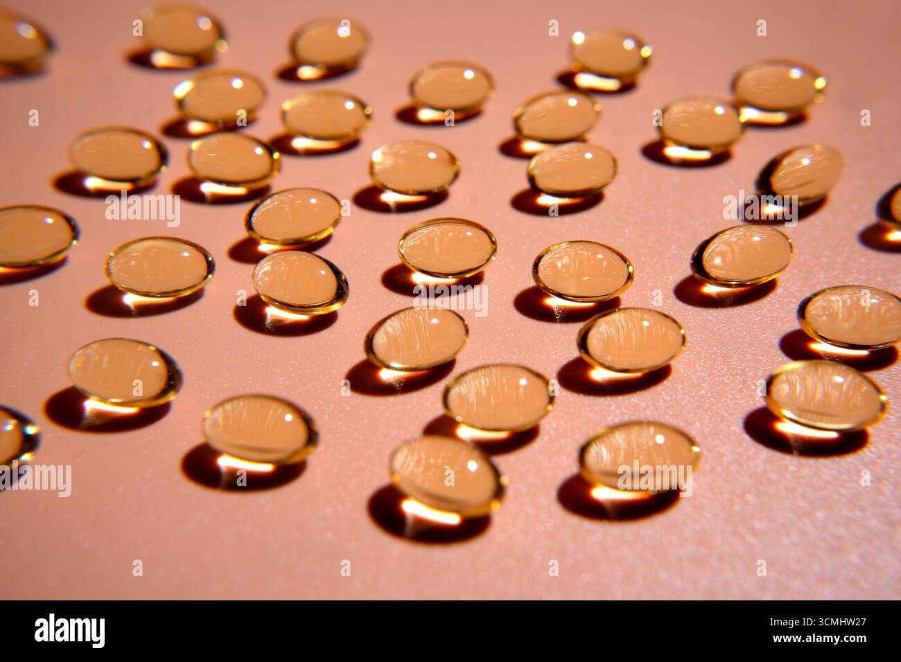 Mehrere goldene Vitaminpillen werfen Schatten auf rosa Hintergrund und schaffen ein optisch ansprechendes Muster Stockfoto