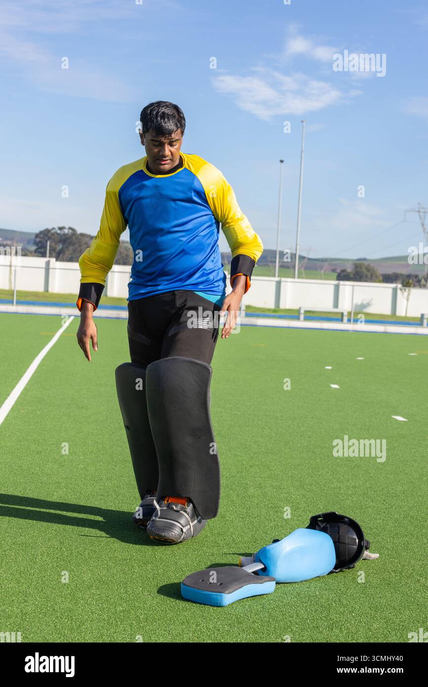Asiatisch-indischer Teenager, der auf dem Rasenfeld mit Beinschutz und Helm, Trittpolster läuft Stockfoto