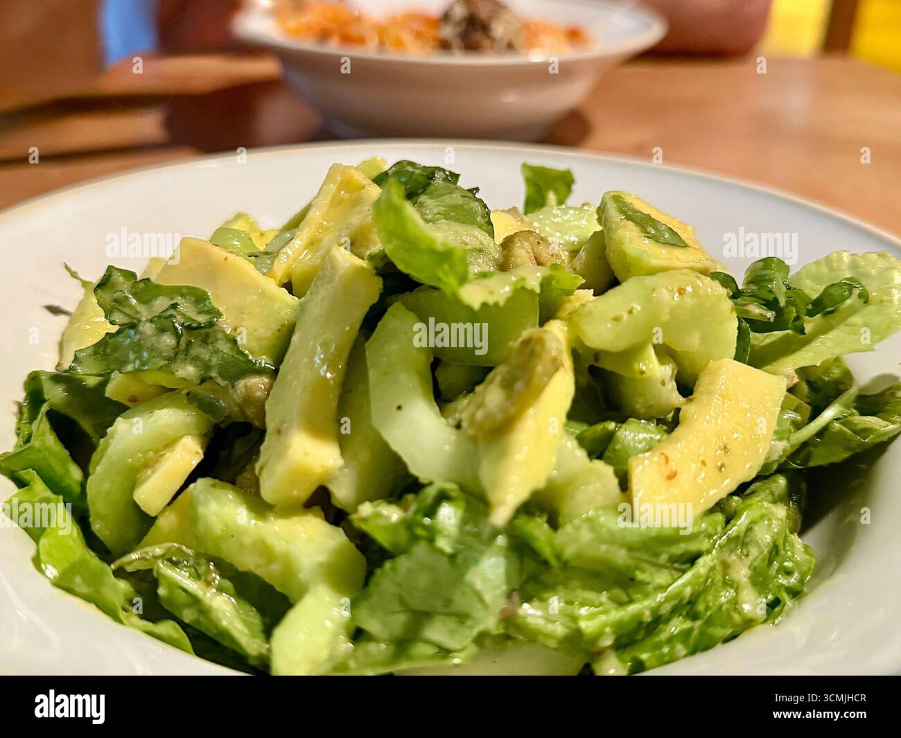 Nahaufnahme eines Salats mit Avocado, Gurke und olivgrünem Salat mit einer Schüssel Nudeln im Hintergrund Stockfoto