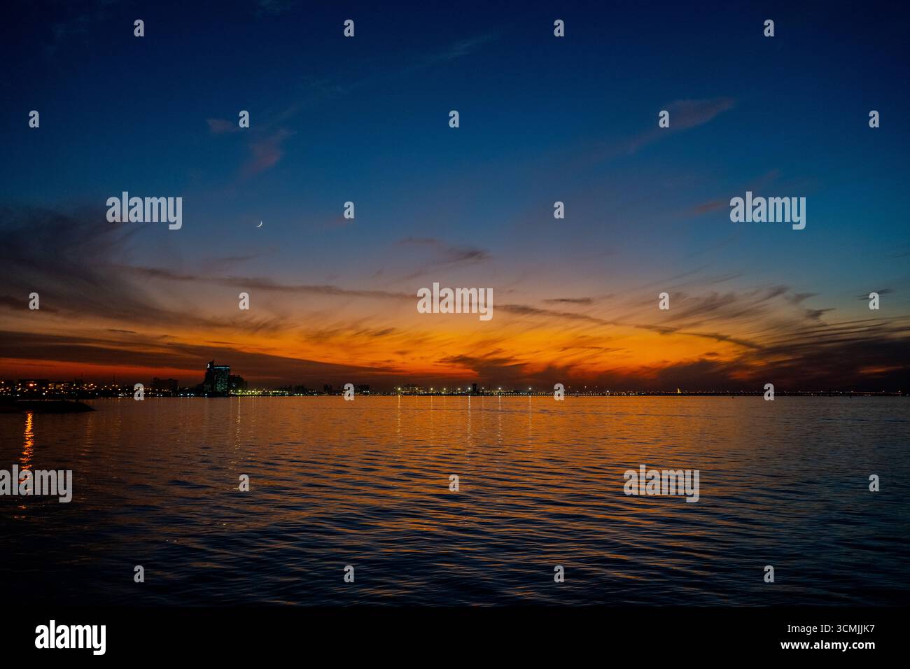 Sonnenuntergang über dem Arabischen Golf mit Kuwait City Lichtern, die sich auf dem Wasser spiegeln, wenn sich die Nacht nähert. Kuwait City, Kuwait. Stockfoto