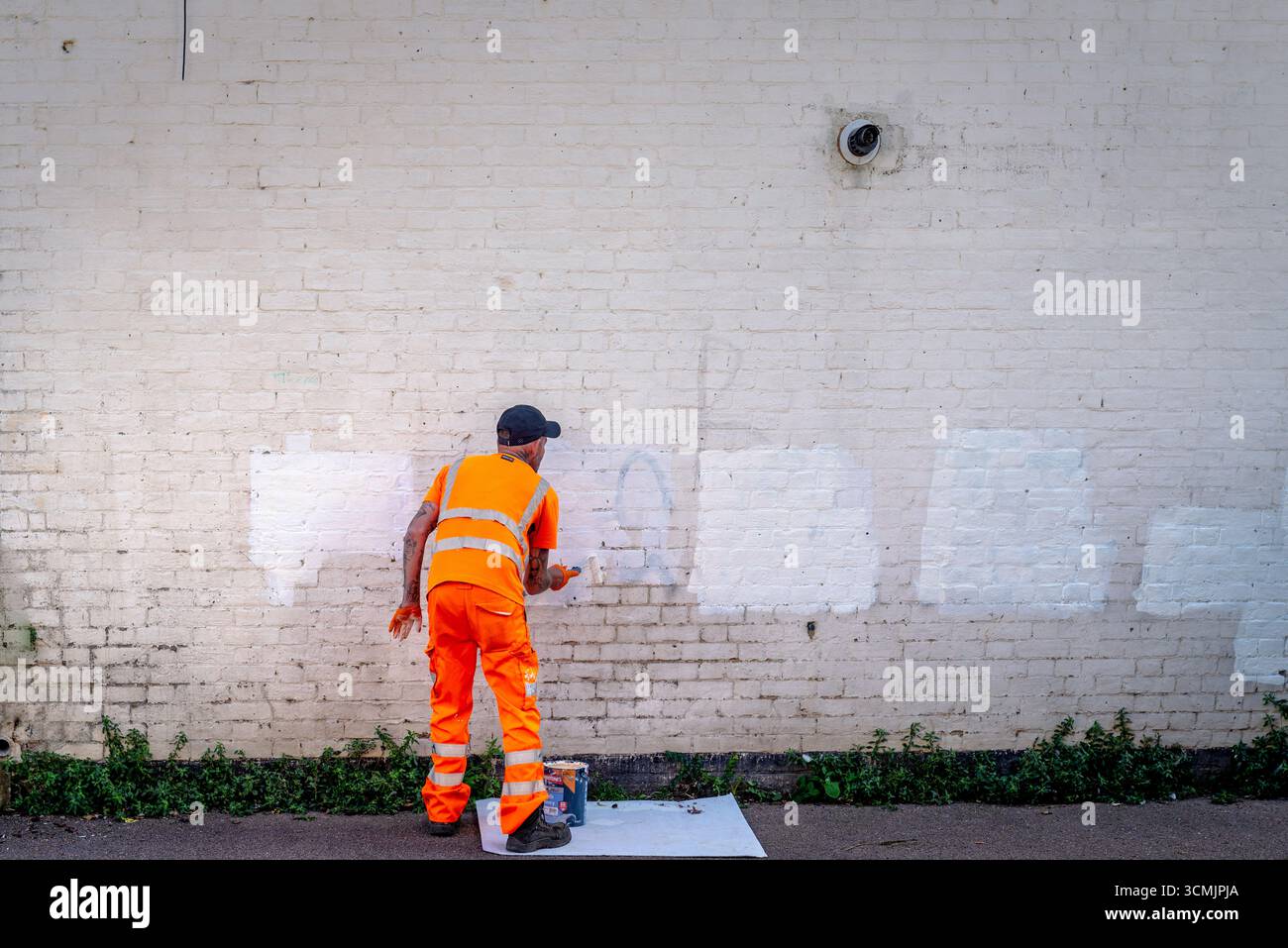 Gemeindearbeiter in High-Visibility-Kleidung, die über Graffiti auf einer Ziegelwand malt Stockfoto