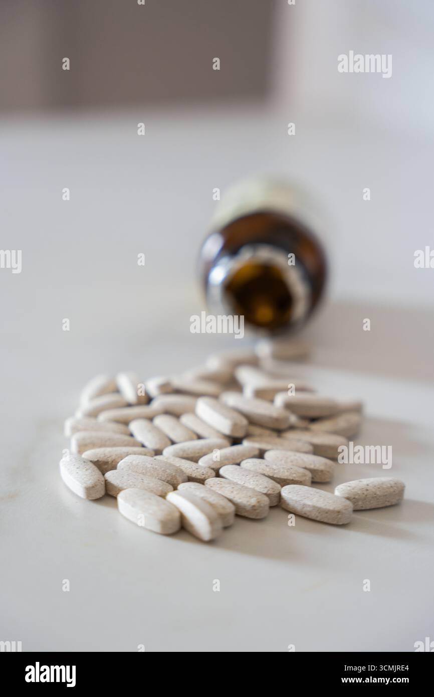 Vertikales Bild von medizinischen Pillen verschüttet von einer braunen Flasche auf einen weißen Tisch, die Gesundheit, Medizin und Behandlung darstellen Stockfoto