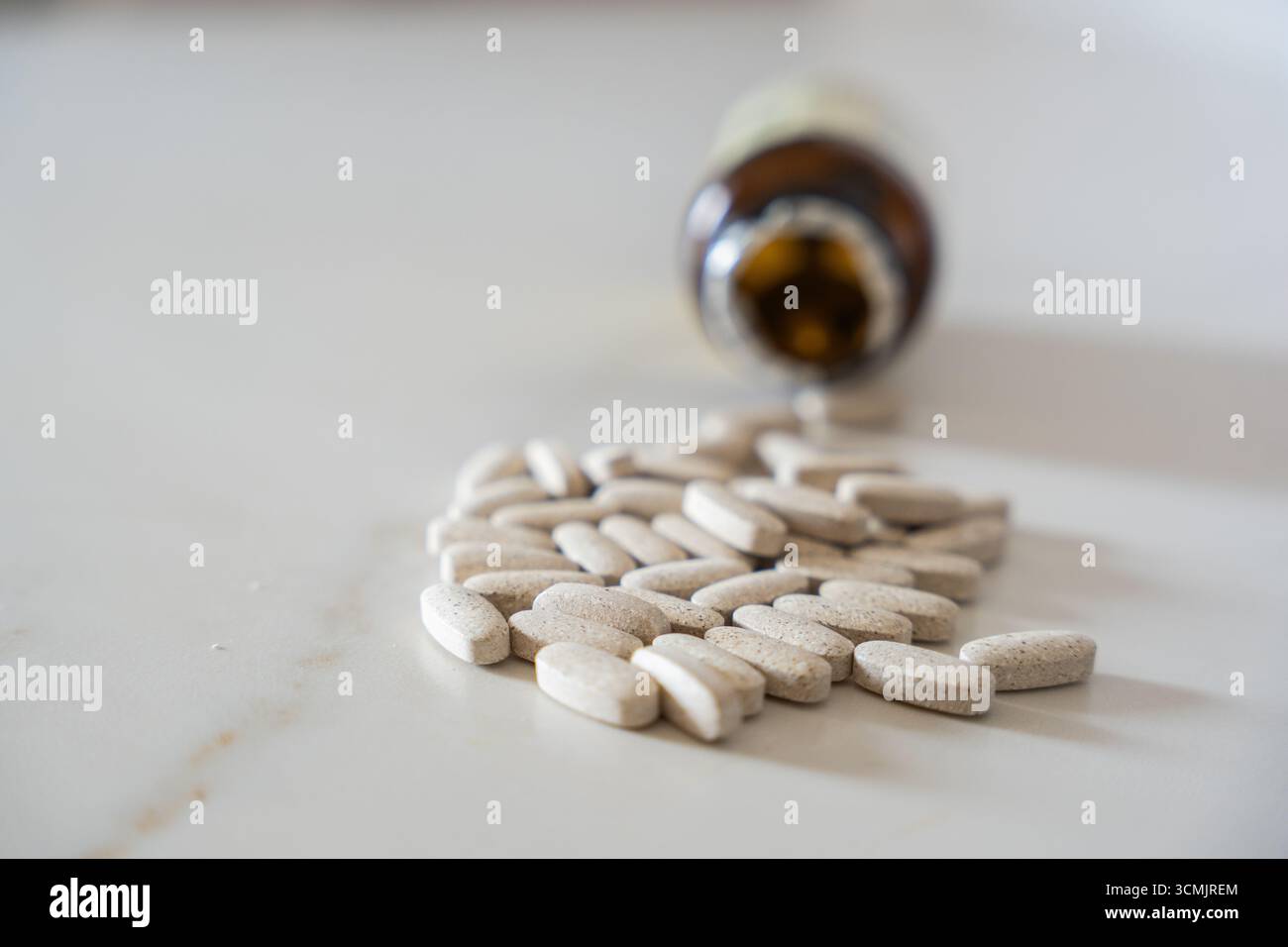Medizinische Pillen werden aus einer braunen Flasche auf einen weißen Tisch verschüttet und stehen für Gesundheit, Medizin und Behandlung Stockfoto