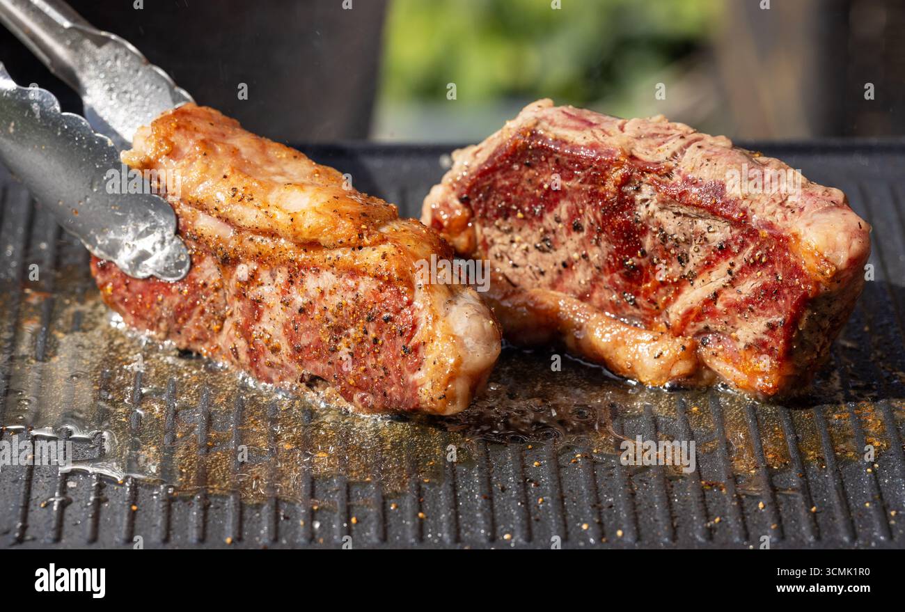 Frisch gegrillte Rinderstriploin-Steaks auf heißer elektrischer Grilloberfläche Stockfoto