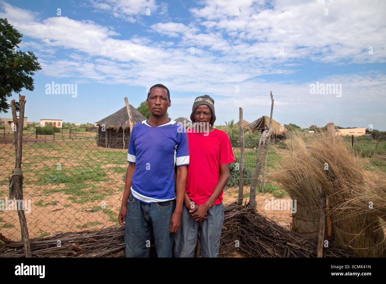 Dorf zwei afrikanische Männer, stehend im Hof, im Hintergrund Hütte mit Strohdach und blauem Himmel, Südafrika, Stockfoto