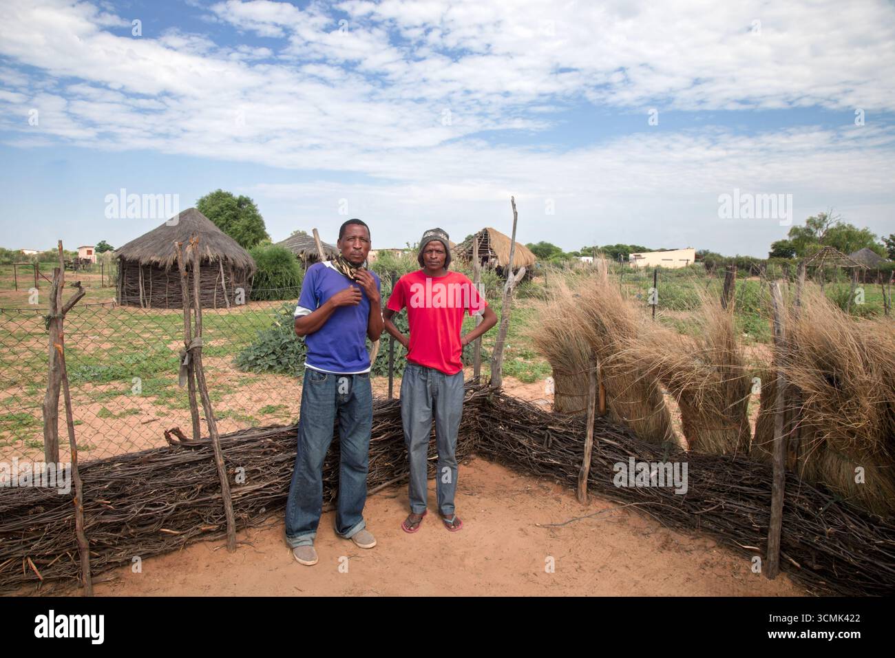 Dorf zwei afrikanische Männer, stehend im Hof, im Hintergrund Hütte mit Strohdach und blauem Himmel, Südafrika, Stockfoto