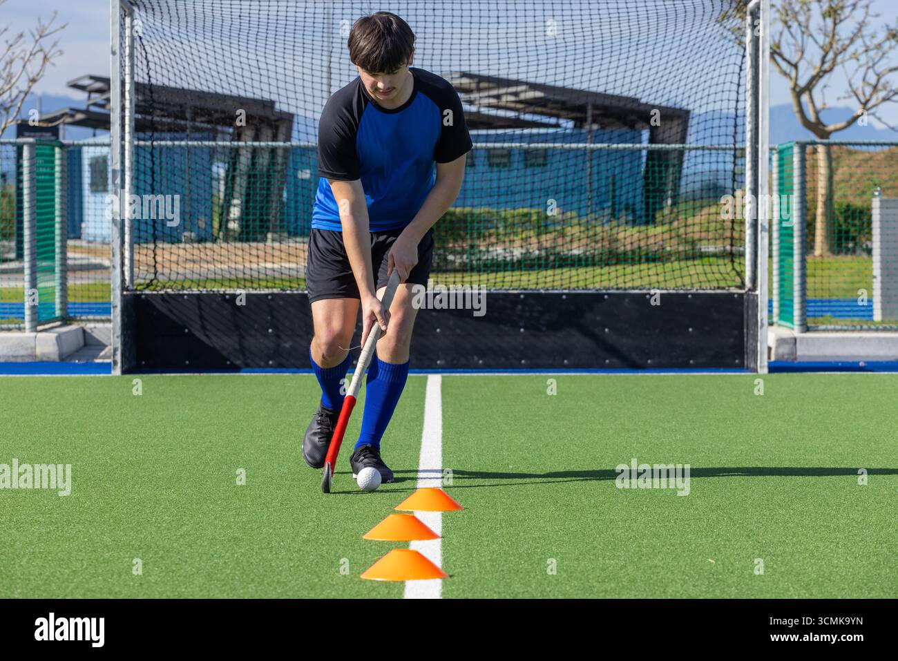 Athlet dribbelt Feldhockeyball auf hellgrünem Rasen mit Kegeln im Freien Stockfoto