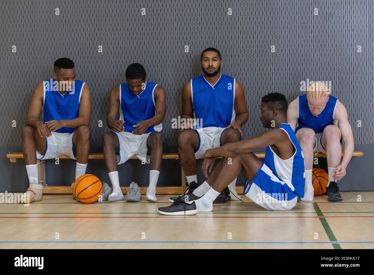 Verschiedene männliche Basketballmannschaften passen Turnschuhe auf der Bank im Fitnessstudio in der Nähe von Basketbälle an Stockfoto