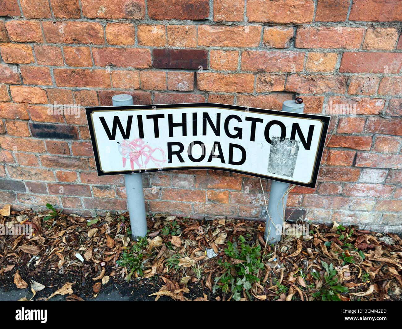 Verwittertes Withington Road Schild auf einem Gehweg in der Nähe einer Ziegelmauer in Manchester. Stockfoto