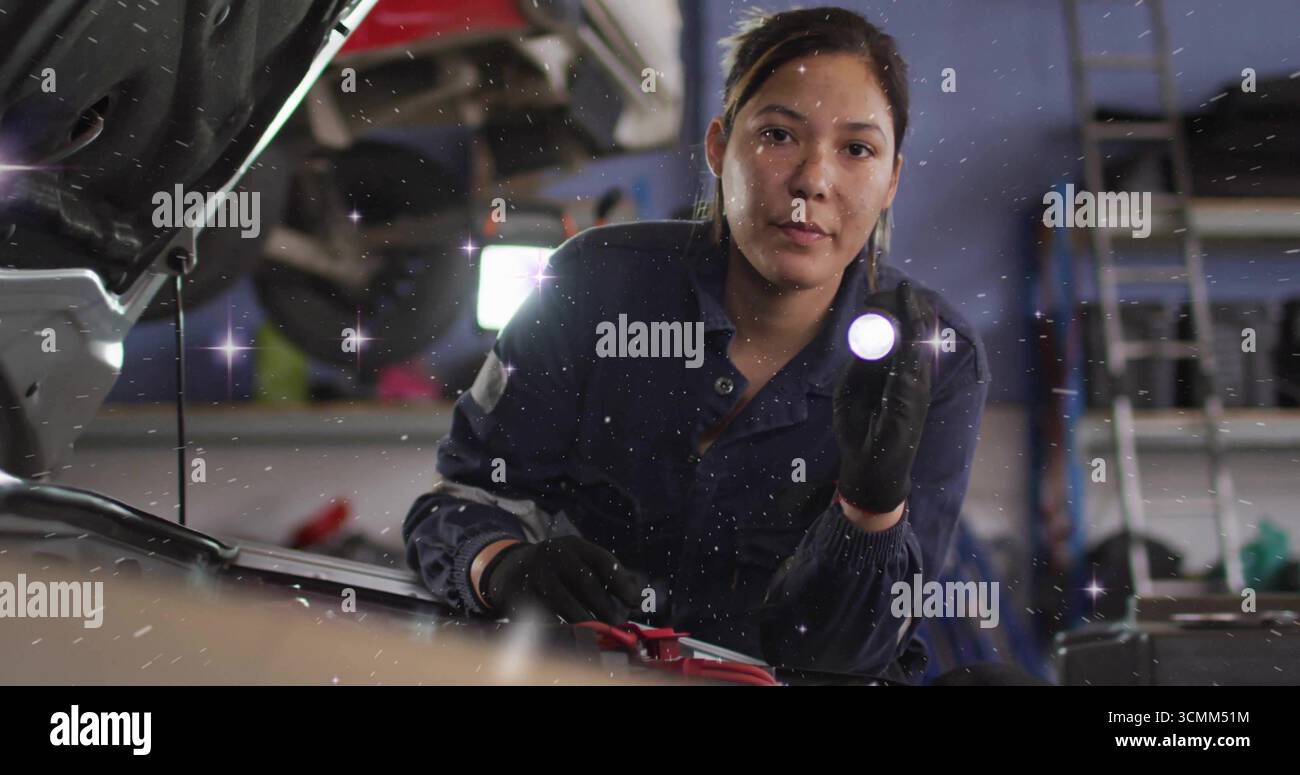 Kniende Mechanikerin in Overalls, die den Motor in der Werkstatt überprüft, Taschenlampen Beleuchtung Überbrückungsklammern Stockfoto