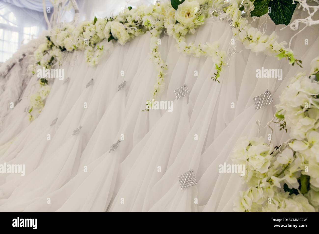 Die atemberaubende Hochzeitskulisse bietet fließende weiße Vorhänge mit zartem Grün und frischen weißen Blumen. Das Arrangement ist klein eingerichtet Stockfoto