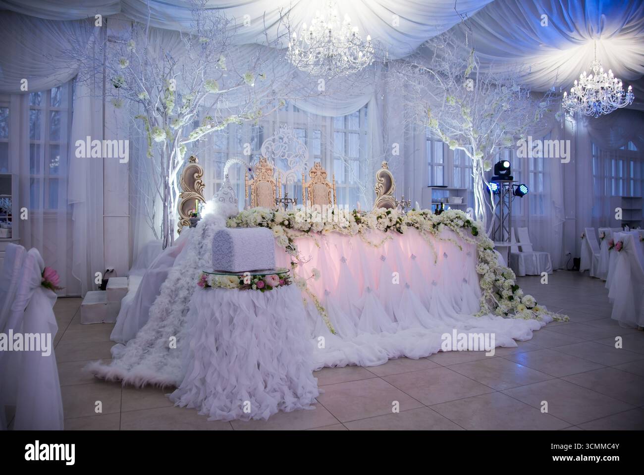 Ein wunderschöner Hochzeitsempfang findet in einem geräumigen Bankettsaal statt, der mit weichen, weißen Vorhängen und funkelnden Kronleuchtern dekoriert ist. Stockfoto