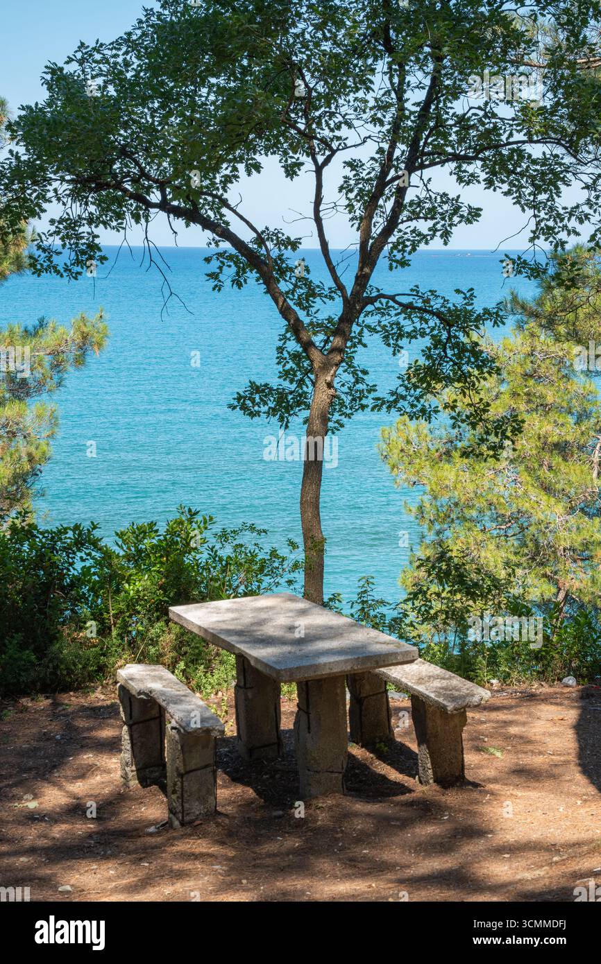 Picknicktisch aus Stein mit Blick auf das klare blaue Meer. Friedlicher Blick auf das Meer von einem schattigen Ruheplatz Stockfoto