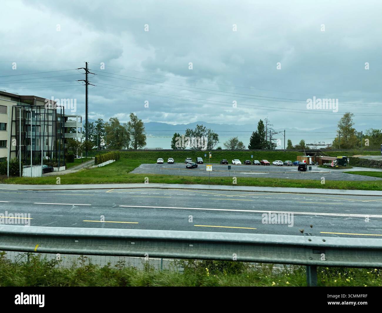 Offener Parkplatz in der Nähe einer Straße mit Blick auf einen See in der Schweiz mit Wolken. Stockfoto