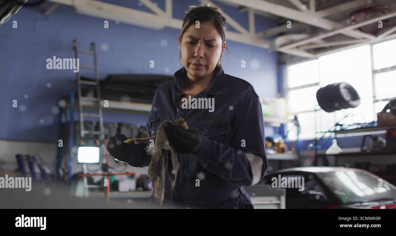 Hispanischer Mechaniker wischt Motorölmessstab mit Lappen in der Autowerkstatt ab, mit Leiter-Reserverad Stockfoto