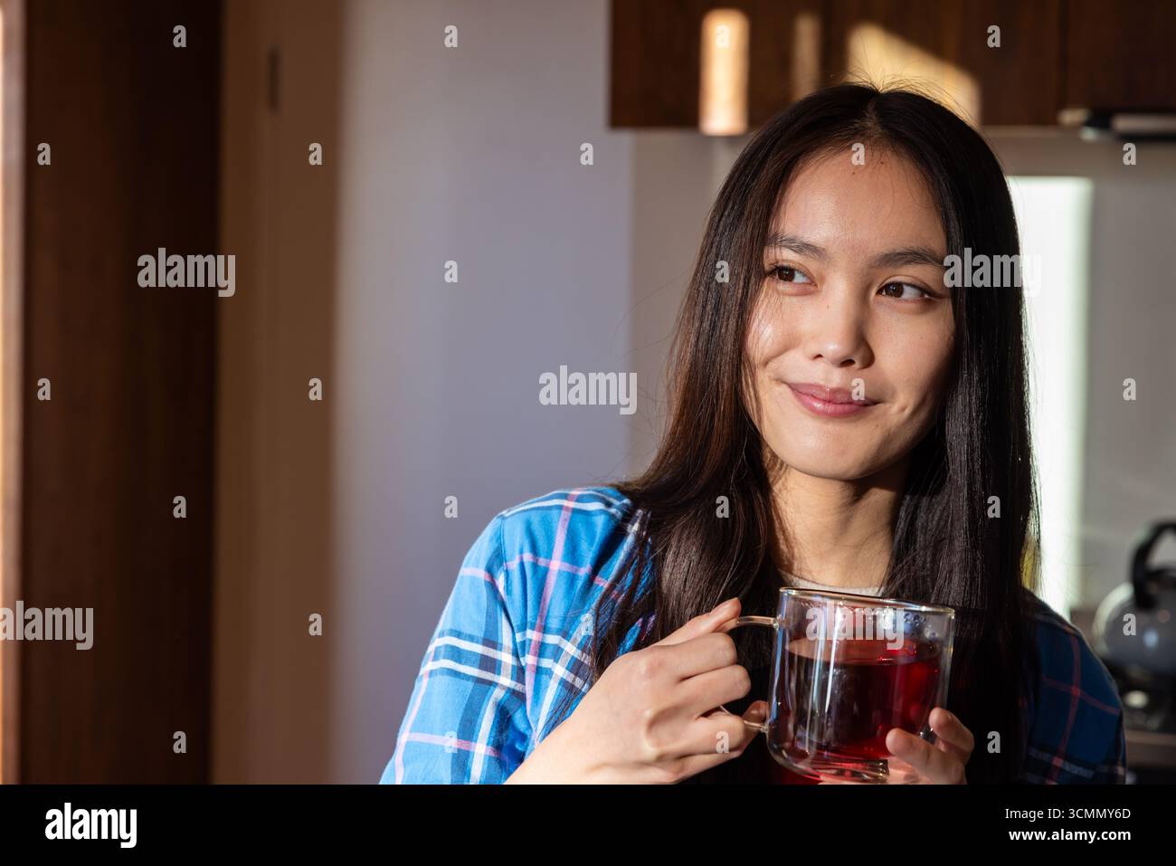 Asiatische Frau mit Glasbecher Tee in der Küche mit Edelstahl-Wasserkocher, Kopierraum Stockfoto