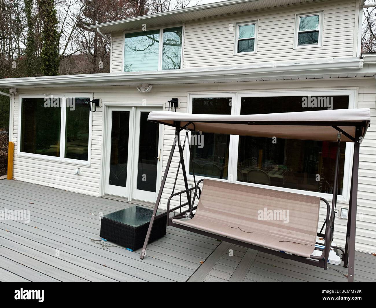 Jenkintown, Pennsylvania, USA - 01. April 2025: Wohnterrasse mit beigefarbenem Schaukelsitz und großen Fenstern Stockfoto