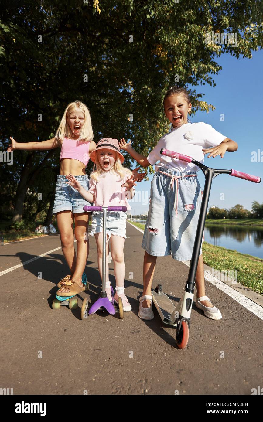 Gruppe fröhlicher Kinder, die an einem sonnigen Sommertag im Freien Roller fahren Stockfoto