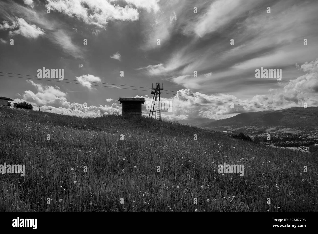 Schwarzweiß-Foto einer alten Seilbahn auf einer Wiese mit dramatischem Himmel. Schöne Kunst ländliche Landschaft, Konzept der Nostalgie, Erbe und Passage Stockfoto