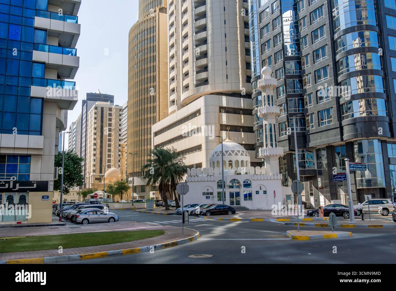 Städtische Kreuzung in Abu Dhabi, VAE, mit modernen Hochhäusern, die an klaren Tagen eine traditionelle weiße Moschee mit Kuppel und Minarett umgeben Stockfoto