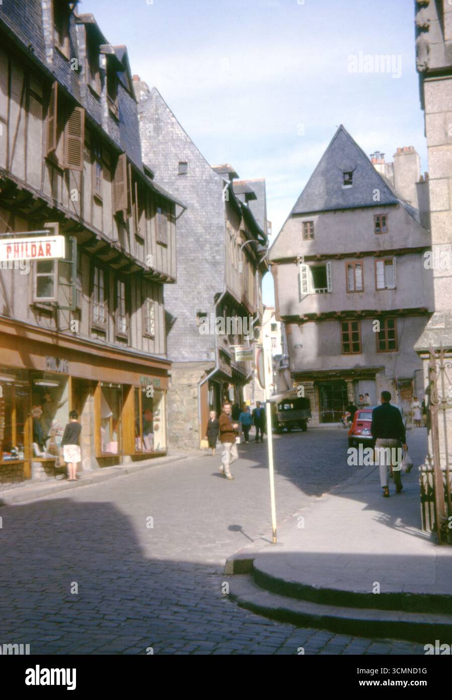 Straßenszene in Dinan, Bretagne, Frankreich, 1963. Fachwerkgebäude mit Schieferdächern, Geschäfte und Fußgänger im historischen Stadtzentrum. Stockfoto